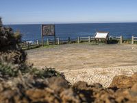 a small stone pathway to a beach with rocks and a wooden sign board in the foreground