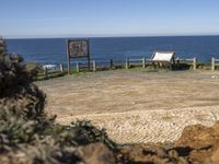 a small stone pathway to a beach with rocks and a wooden sign board in the foreground