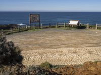 a small stone pathway to a beach with rocks and a wooden sign board in the foreground