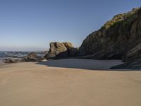 a man riding a surfboard on top of a sandy beach next to a rocky cliff