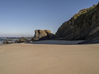 a man riding a surfboard on top of a sandy beach next to a rocky cliff