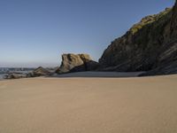 a man riding a surfboard on top of a sandy beach next to a rocky cliff