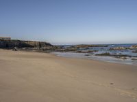 footprints along the sand at the ocean beach in front of rocks and cliffs along the coastline