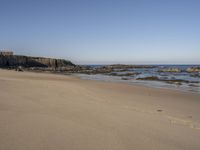 footprints along the sand at the ocean beach in front of rocks and cliffs along the coastline