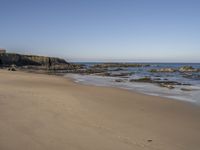 footprints along the sand at the ocean beach in front of rocks and cliffs along the coastline