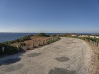 the path to a beach leading to a road and some water in the distance with a blue sky