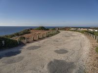 the path to a beach leading to a road and some water in the distance with a blue sky