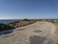 the path to a beach leading to a road and some water in the distance with a blue sky