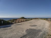 the path to a beach leading to a road and some water in the distance with a blue sky