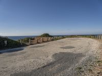 the path to a beach leading to a road and some water in the distance with a blue sky