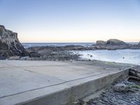 a skateboarder stands on the edge of a stone ramp overlooking the ocean at twilight