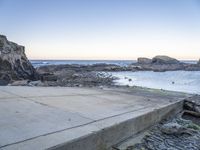 a skateboarder stands on the edge of a stone ramp overlooking the ocean at twilight