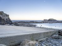 a skateboarder stands on the edge of a stone ramp overlooking the ocean at twilight