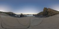 a large fish eye lens in front of rocks and water at the beach on a beautiful day