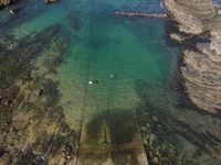 a bird's eye view of clear waters near an island with rocks and a sailboat