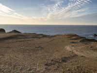 a person standing on top of a sandy hill near water and cliffs and clouds above