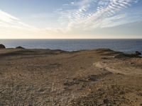 a person standing on top of a sandy hill near water and cliffs and clouds above