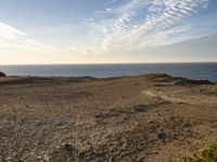 a person standing on top of a sandy hill near water and cliffs and clouds above