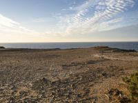 a person standing on top of a sandy hill near water and cliffs and clouds above