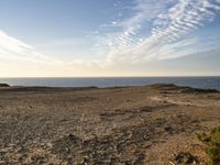 a person standing on top of a sandy hill near water and cliffs and clouds above