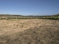 a dirt field with dirt on the ground with a fence and a horse standing in front of it