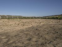 a dirt field with dirt on the ground with a fence and a horse standing in front of it