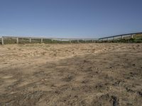 a dirt field with dirt on the ground with a fence and a horse standing in front of it