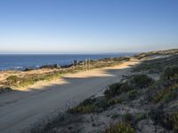 a dirt road by a body of water near a beach with a bench on the side