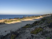 a dirt road by a body of water near a beach with a bench on the side