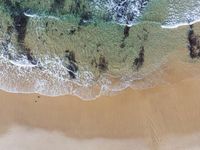 an aerial view of the shore with waves crashing and swimmers walking in the water below