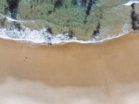 an aerial view of the shore with waves crashing and swimmers walking in the water below