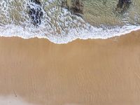 an aerial view of the shore with waves crashing and swimmers walking in the water below