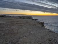 an empty bench is on a cliff above the water in sunset time with sky and clouds