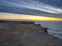 an empty bench is on a cliff above the water in sunset time with sky and clouds