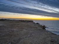 an empty bench is on a cliff above the water in sunset time with sky and clouds