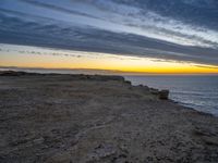 an empty bench is on a cliff above the water in sunset time with sky and clouds