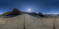 a tripod image of a road and some rocks and water underneath the sun on a clear day