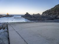 there is a skateboard that is on a paved area near the ocean shore at sunset