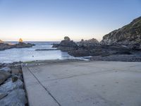 there is a skateboard that is on a paved area near the ocean shore at sunset