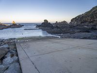 there is a skateboard that is on a paved area near the ocean shore at sunset