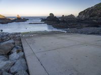 there is a skateboard that is on a paved area near the ocean shore at sunset