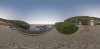 a stone walkway next to beach with buildings in the background, and one being distorted by a fish eye