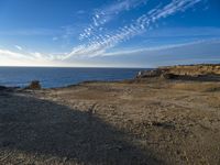 two people walking toward the ocean near a rocky shore, in front of some clouds