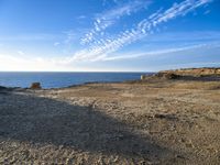 two people walking toward the ocean near a rocky shore, in front of some clouds