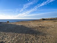 two people walking toward the ocean near a rocky shore, in front of some clouds