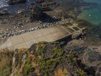 the aerial view of an empty concrete area near the ocean, on a rocky beach