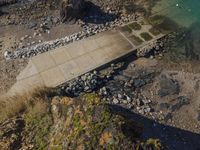 the aerial view of an empty concrete area near the ocean, on a rocky beach