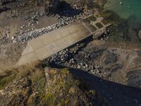 the aerial view of an empty concrete area near the ocean, on a rocky beach