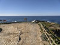 a dirt road with a sign next to the ocean by some wooden fences near a cliff