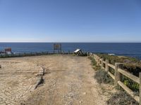 a dirt road with a sign next to the ocean by some wooden fences near a cliff